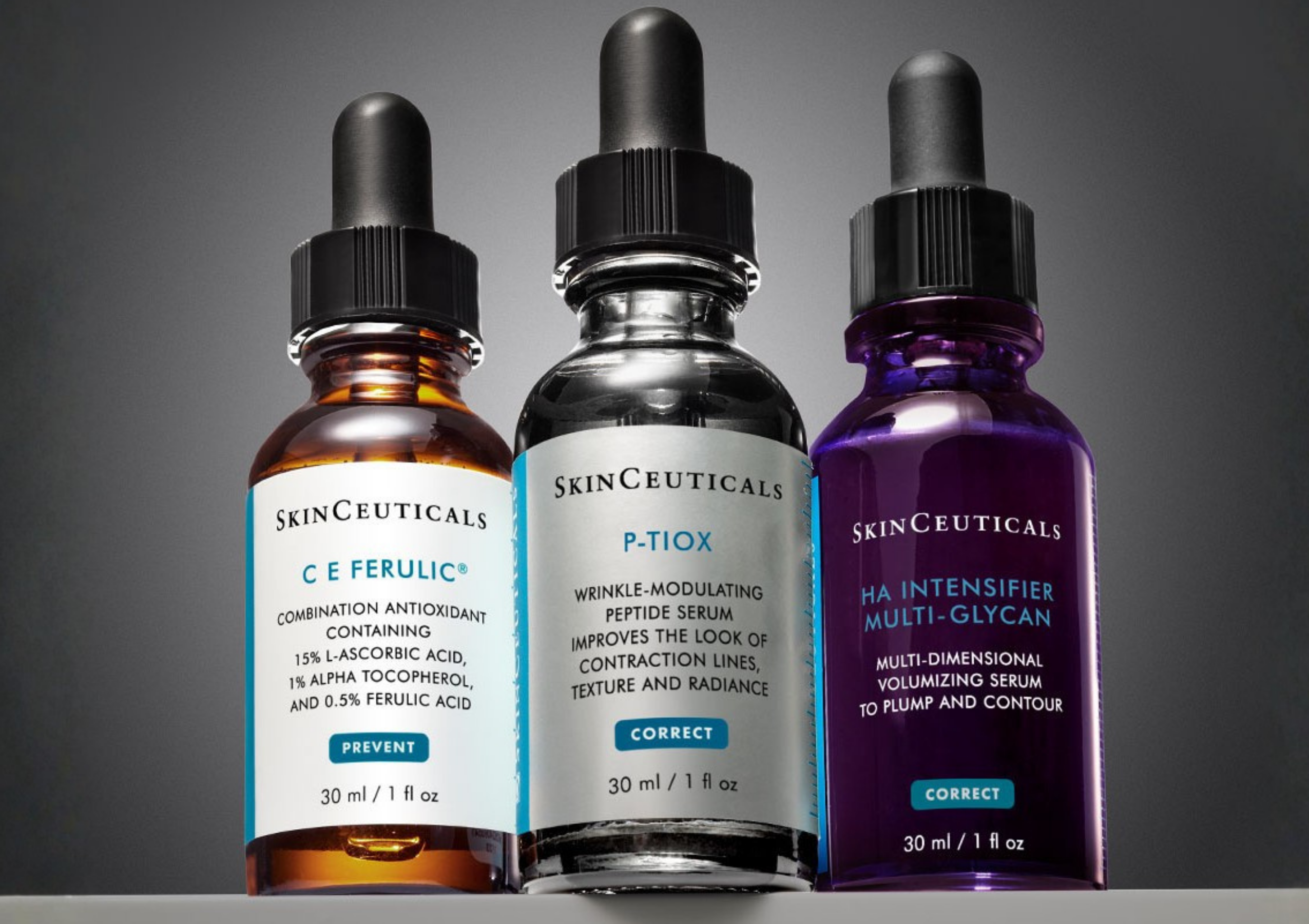 Three SkinCeuticals serum bottles with droppers in orange, clear, and purple glass against a gray background, viewed from the front-inside edge of a display shelf, close-up.